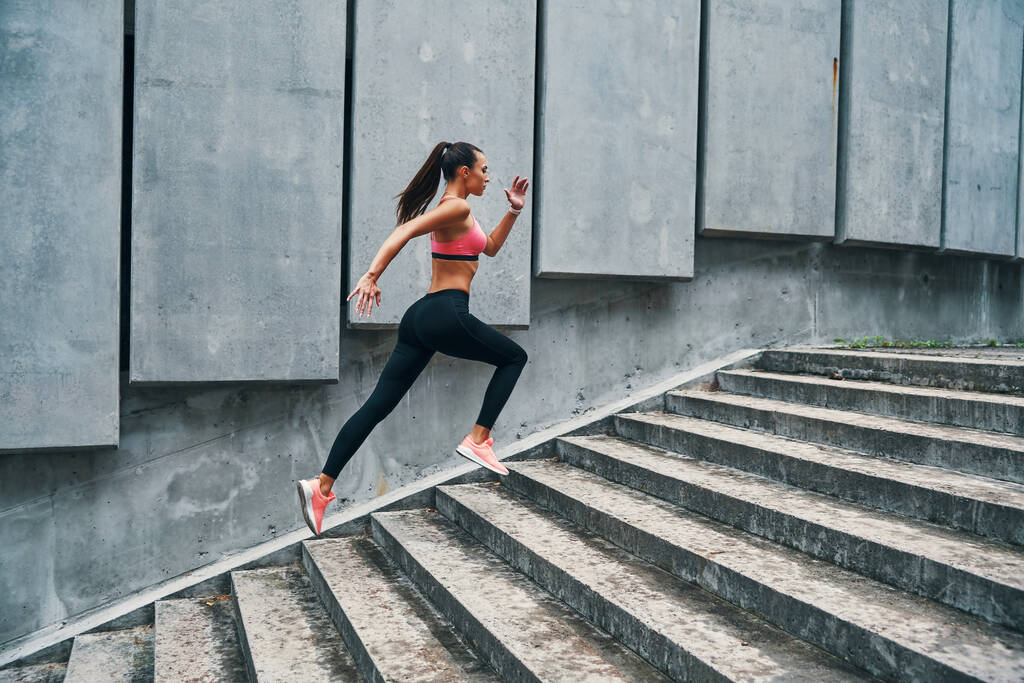 Полная длина молодой женщины в спортивной одежде бег трусцой во время упражнений на ступеньках на улице - Фото, изображение