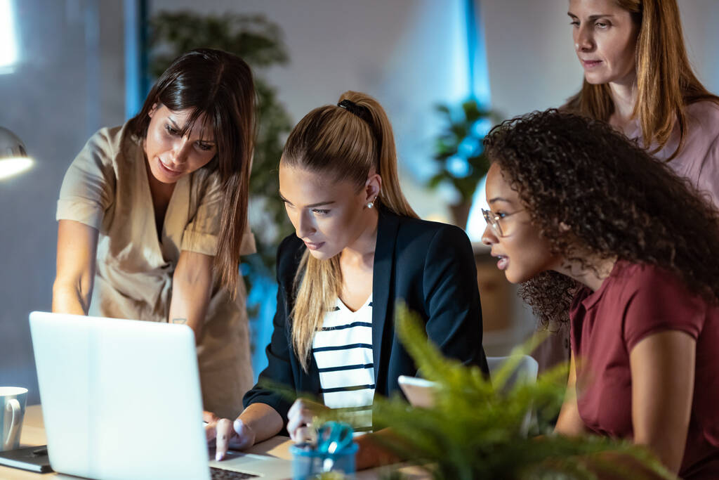 Opname van vier slimme zakenvrouwen die praten en de recentste werkzaamheden op de computer bekijken in een gezamenlijke werkruimte. - Foto, afbeelding
