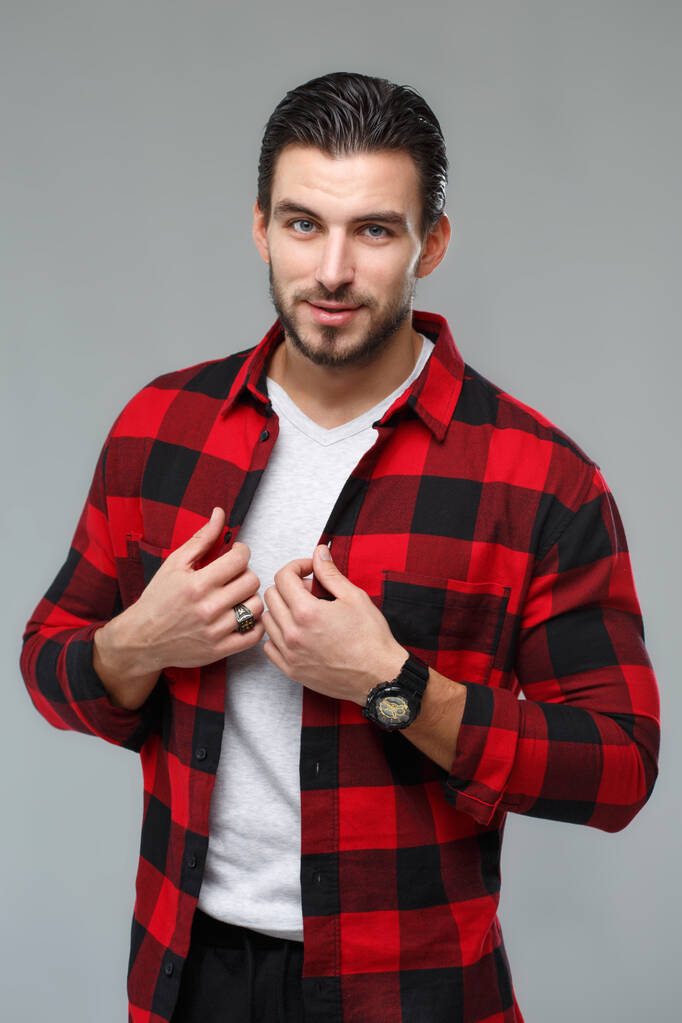 Retrato de un hombre guapo sonriente con estilo en una camisa a cuadros roja y negra aislada sobre fondo gris. - Foto, imagen
