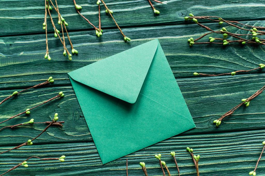 верхний вид деревянного зеленого фона с цветущими ветвями и конвертом - Фото, изображение