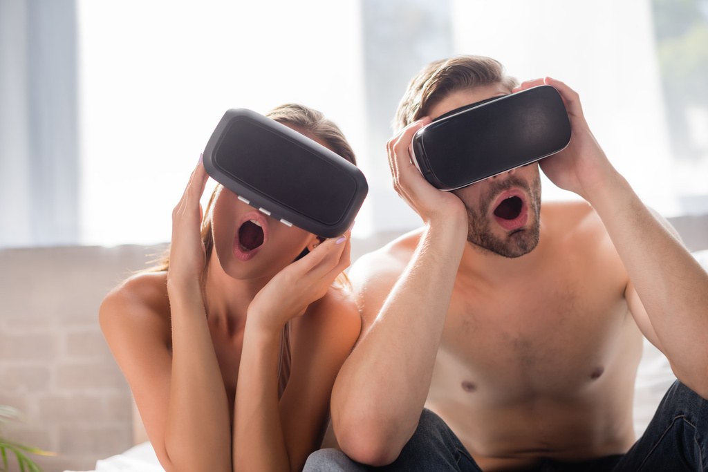 σοκαρισμένο ζευγάρι που αγγίζει ακουστικά VR στην κρεβατοκάμαρα - Φωτογραφία, εικόνα
