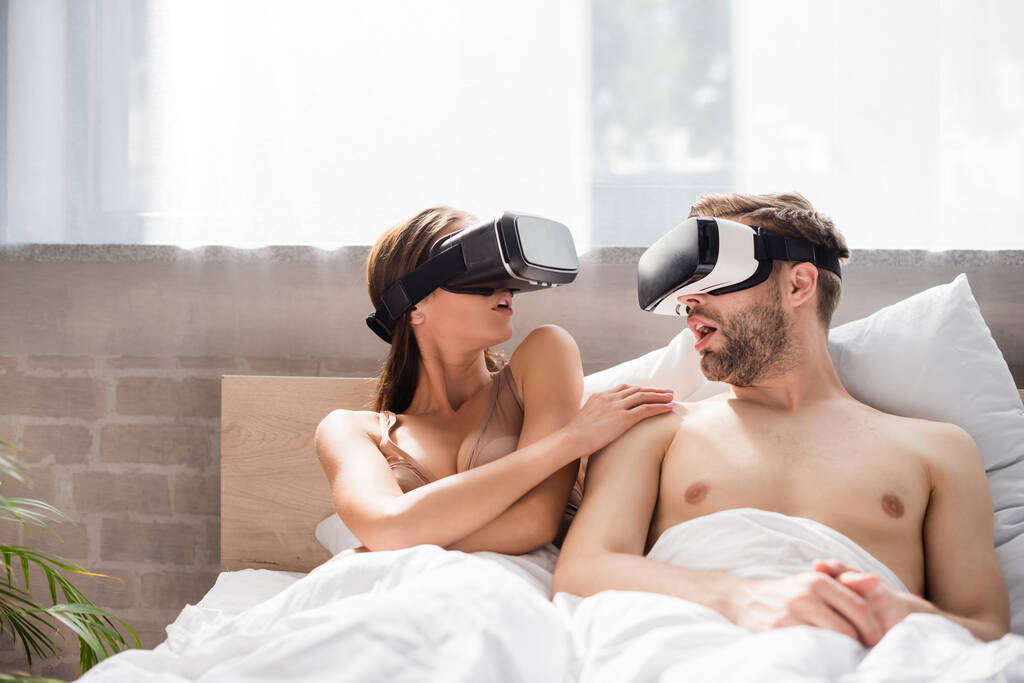 pareja emocionada mirándose mientras están acostados en la cama y usando auriculares vr - Foto, imagen