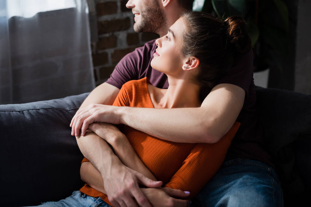 happy young couple embracing while relaxing on sofa and looking away - Photo, Image