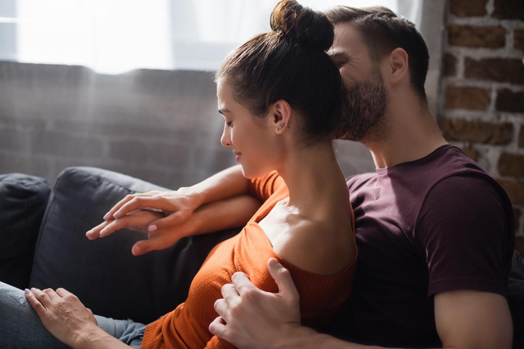 zarter Mann umarmt geliebte Frau, während er zu Hause auf dem Sofa sitzt - Foto, Bild