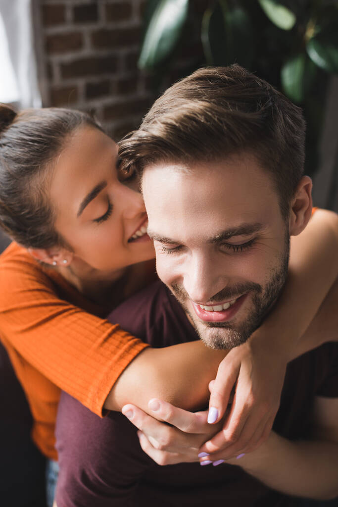 gelukkig vrouw knuffelen nek van glimlachende vriend en fluisteren in zijn oor - Foto, afbeelding