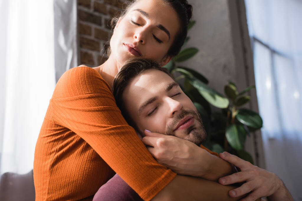 jovem casal abraçando com os olhos fechados enquanto sentado em casa - Foto, Imagem