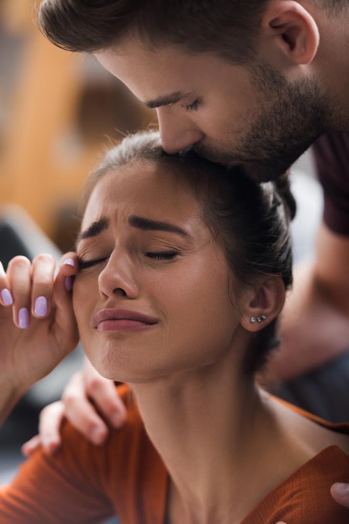 réactif homme baisers tête de pleurer copine essuyant des larmes avec main - Photo, image