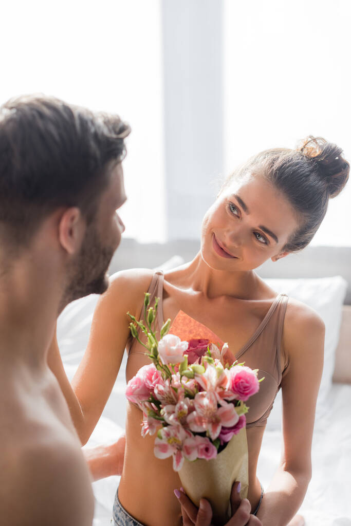 boldog, szexi nő kezében virágok és nézi a férfi homályos előtérben - Fotó, kép