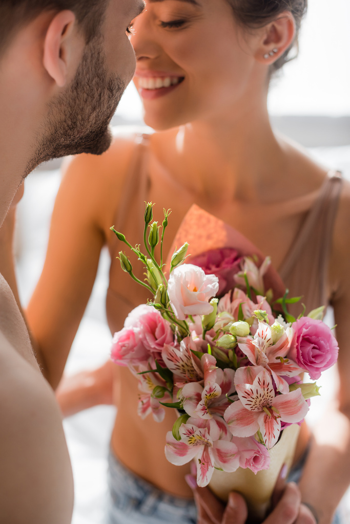 Мужчина, держащий цветы рядом с улыбающейся сексуальной девушкой на размытом фоне - Фото, изображение
