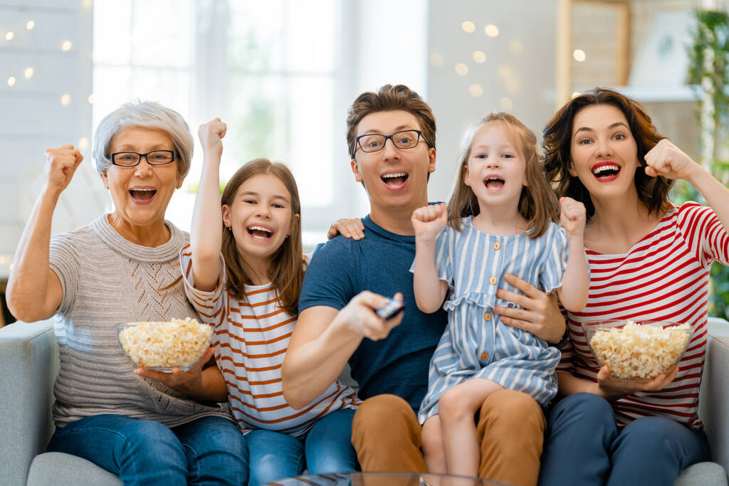 Gelukkige familie kijkend naar projector, TV, films met popcorn thuis. Grootmoeder, moeder, vader en dochters die samen tijd doorbrengen. - Foto, afbeelding