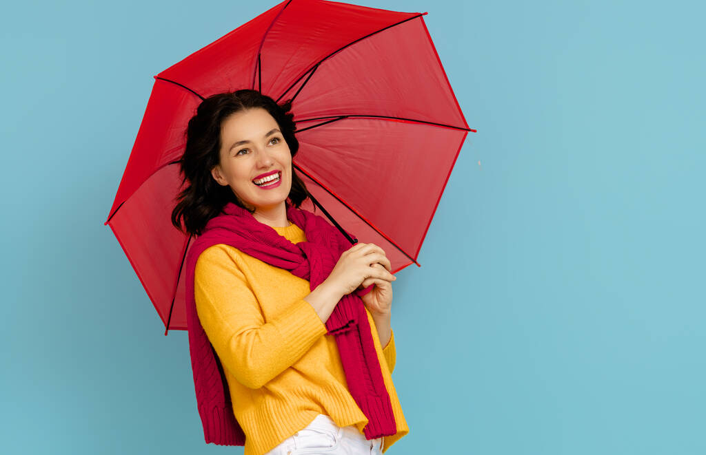 Happy emotional young woman laughing with red umbrella on color teal background. - Photo, Image