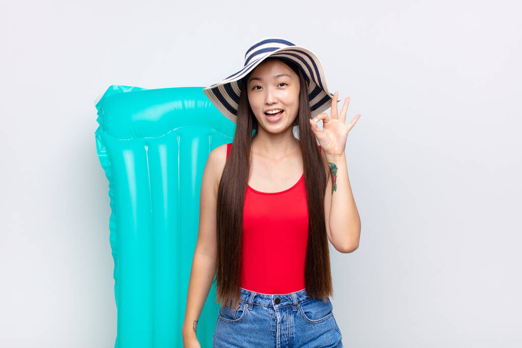aziatische jonge vrouw voelt zich succesvol en tevreden, glimlachen met de mond wijd open, het maken van oke teken met de hand. zomerconcept - Foto, afbeelding