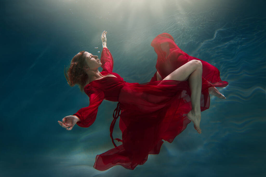 Una chica delgada en un vestido largo rojo nada bajo el agua. - Foto, Imagen