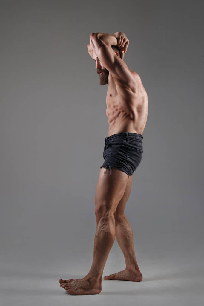 いくつかのショートパンツのアスレチック筋肉の男は灰色の背景に隔離された完全な成長に立っている. - 写真・画像