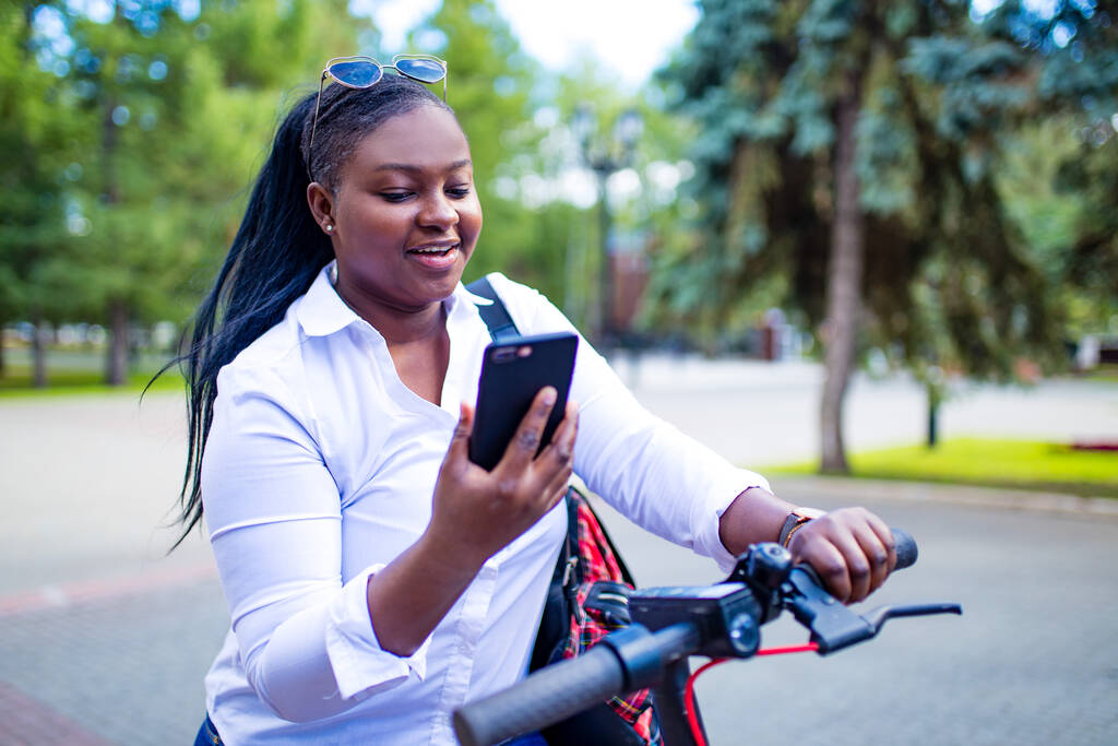 afro femme américaine activer et prépayer une location e-scooter ou un e-vélo dans la rue - Photo, image