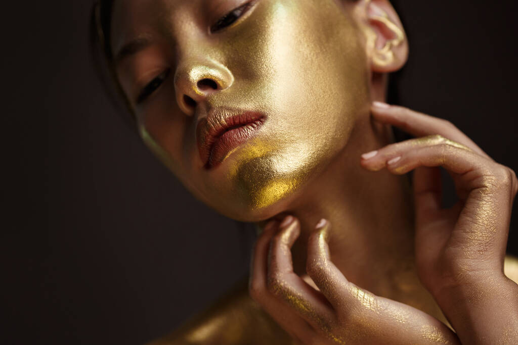 Retrato de belleza de una hermosa chica asiática con pintura dorada en su cara sobre un fondo oscuro. - Foto, Imagen