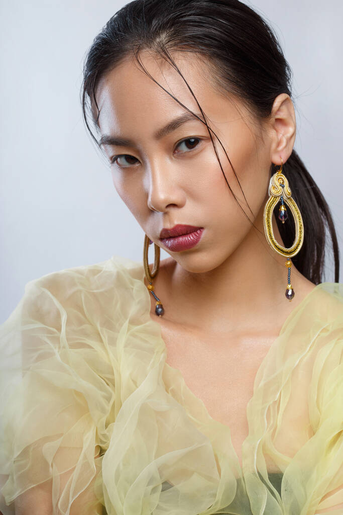 Güzel Asyalı bir kızın zarif portresi. Büyük zarif küpeleri ve sarı havadar kıyafetleri var.. - Fotoğraf, Görsel
