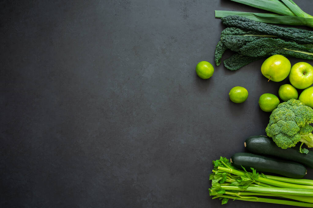 Bovenaanzicht van selderij, courgette, boerenkool, broccoli, prei, appels en limoenen. Groene groenten op zwarte achtergrond met kopieerruimte. Vegetarische levensstijl. - Foto, afbeelding