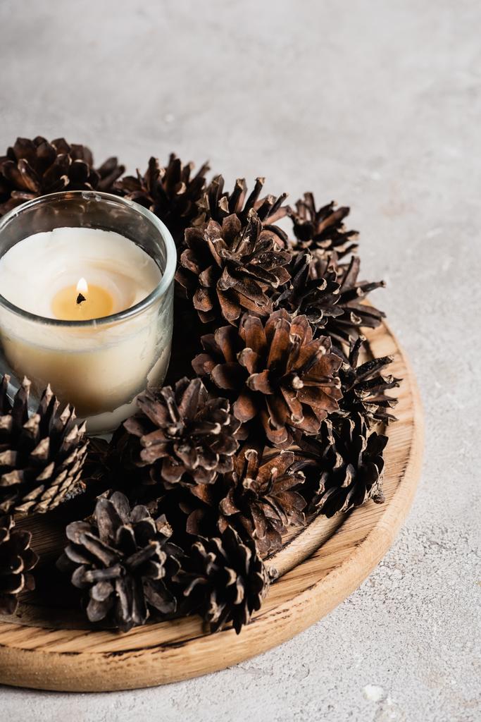 Bougie parfumée avec cônes de pin sur plaque de bois sur fond texturé et gris - Photo, image