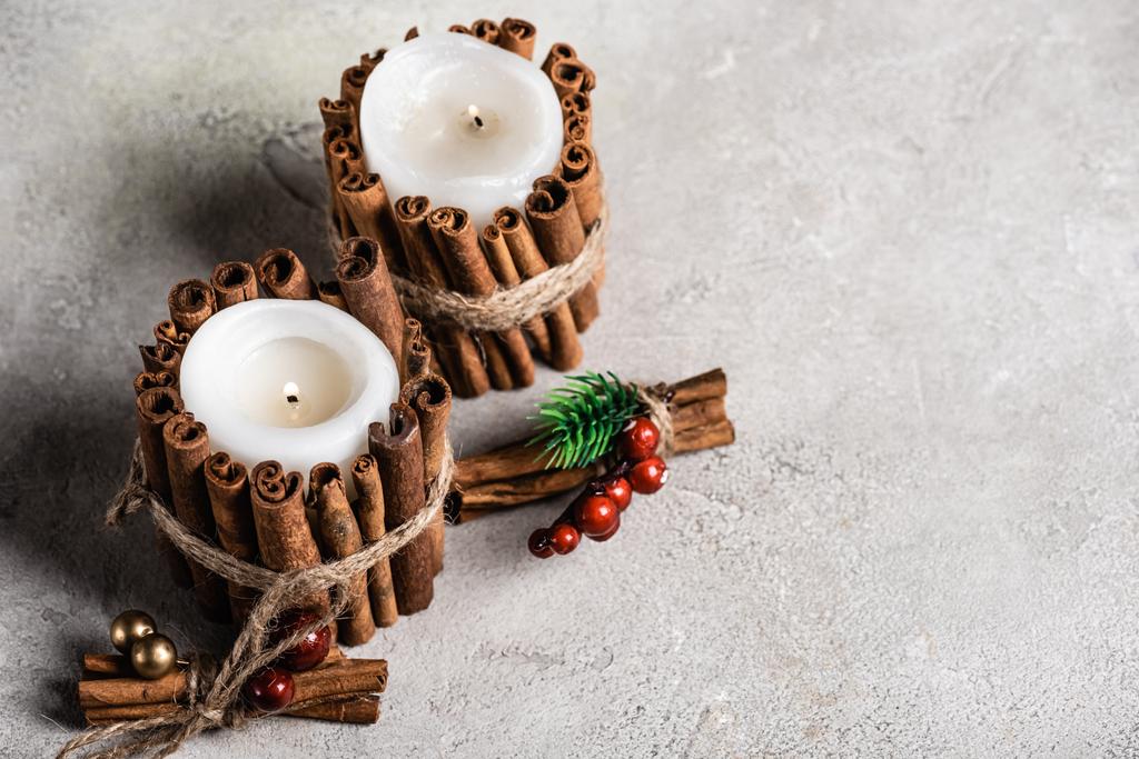 Scented candles decorated with cinnamon sticks on grey and textured background - Photo, Image