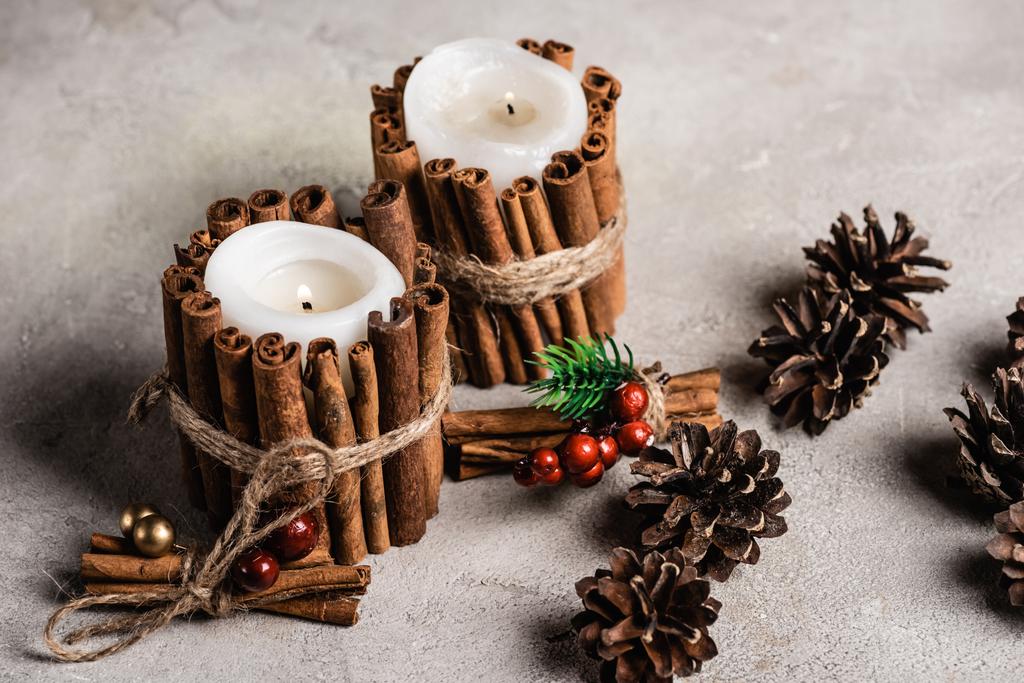 Decorated scented candles near pine cones on textured and grey background - Photo, Image