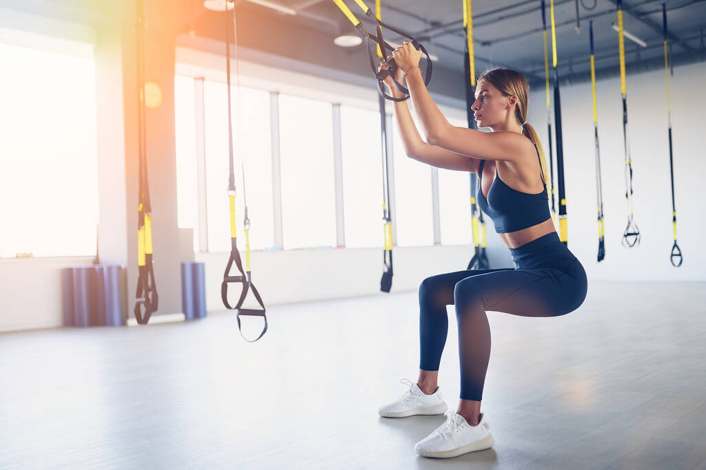 Красивая молодая женщина тренируется с тренером подвески стропы или подвески ремни в тренажерном зале. Концепция верхних упражнений тела на TRX - Фото, изображение