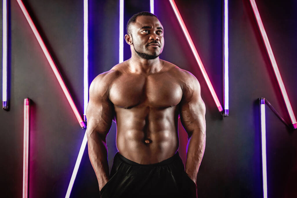 Африканский спортсмен демонстрирует мышцы на фоне флуоресцентных ламп - Фото, изображение