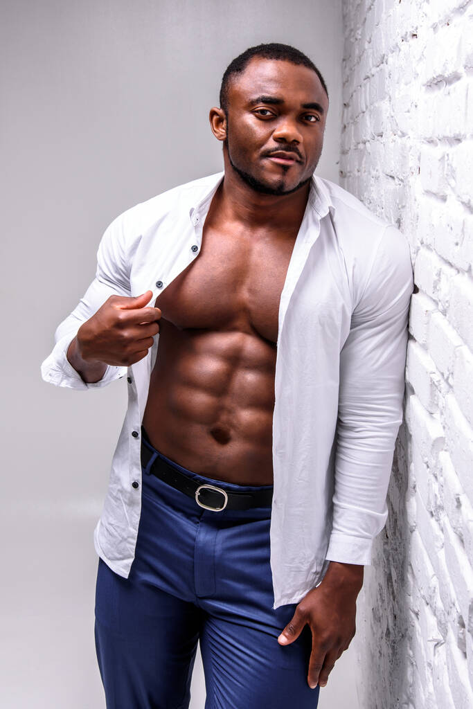 Athlète africain fort en chemise blanche. Poser montrant une forme musculaire parfaite près d'un mur de briques blanches - Photo, image