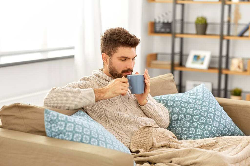 zieke jongeman in deken drinken hete thee thuis - Foto, afbeelding