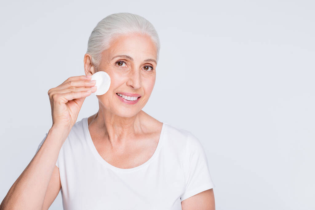 Portrait of charming grandmother holding cotton sponge remove cosmetics wearing white stylish trendy t-shirt isolated over white background - Photo, Image