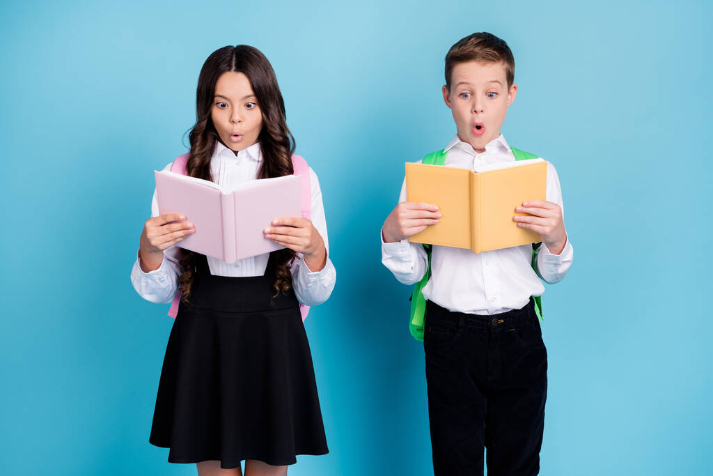 Kuva kaksi pientä tyttö poika koulupoika parhaita ystäviä luokkatoverit hämmästynyt lukea uusia kova matematiikka kohta kulumista reppu valkoinen paita musta housut mekko eristetty sininen väri tausta - Valokuva, kuva