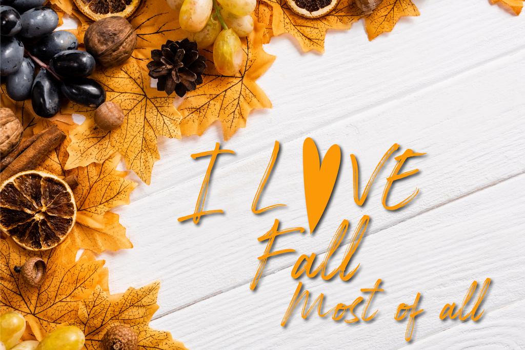 Top view of autumnal decoration and grapes near i love fall most of all lettering on white wooden background - Фото, изображение