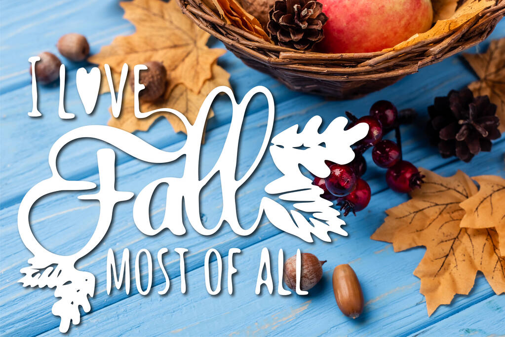 Autumnal leaves, berries, acorns and cones near i love fall most of all lettering on blue wooden background - Фото, изображение