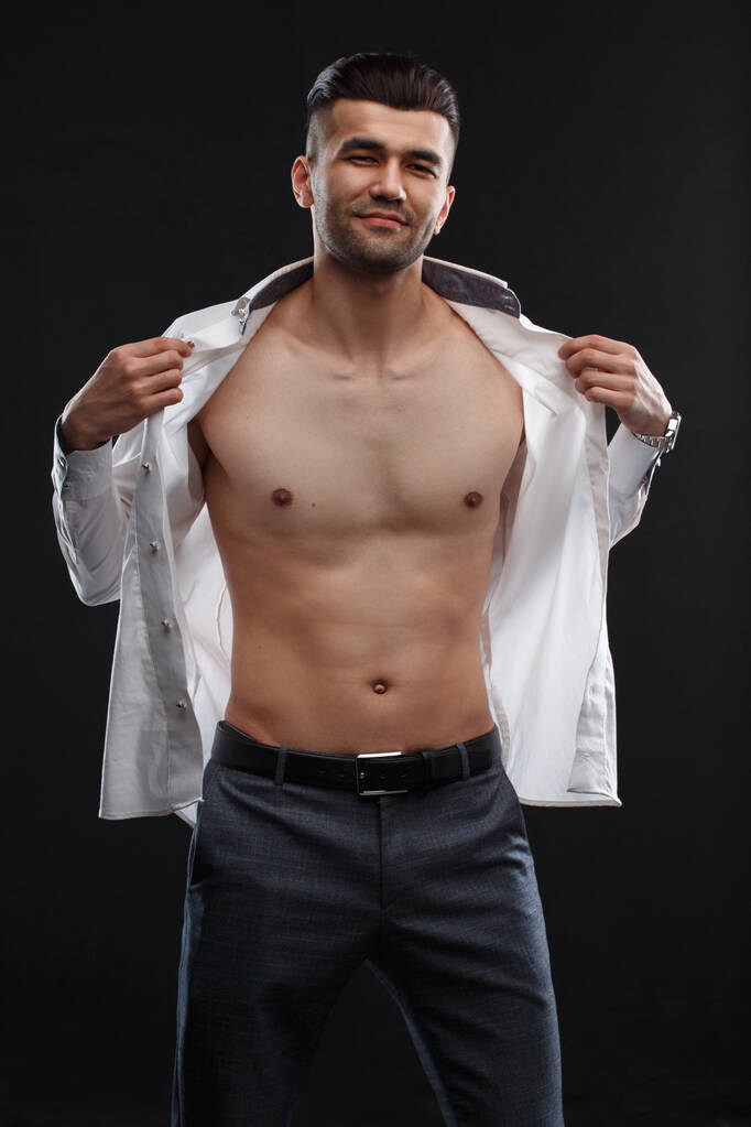 Charismatic sexy man takes off white shirt isolated on black background. - Photo, Image