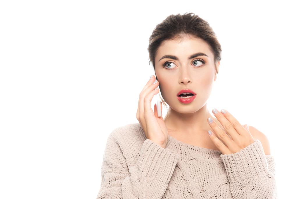 femme surprise en pull tricoté tendance parlant sur smartphone tout en tenant la main près du visage isolé sur blanc - Photo, image