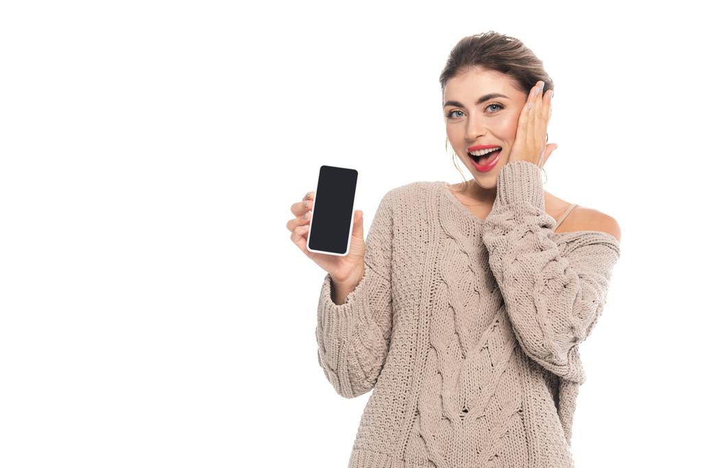 opgewonden vrouw tonen smartphone met leeg scherm terwijl het aanraken van gezicht geïsoleerd op wit - Foto, afbeelding
