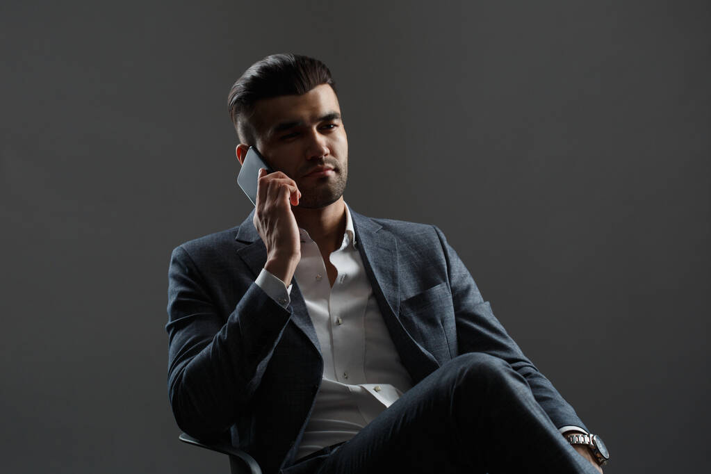 Joven hombre asiático en un traje de negocios hablando por teléfono aislado sobre un fondo gris. - Foto, imagen