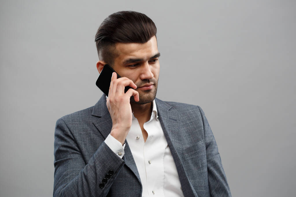 Mladý asijský muž v obchodním obleku mluvit po telefonu izolované na šedém pozadí. - Fotografie, Obrázek