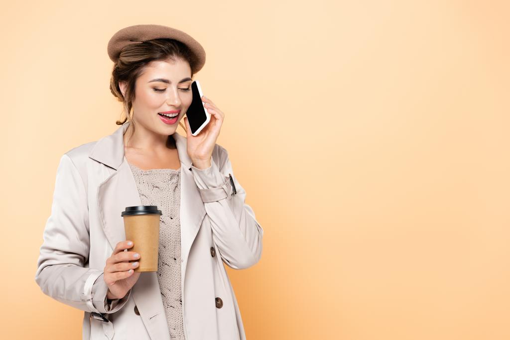 femme à la mode en tenue d'automne parler sur téléphone portable tout en tenant du café pour aller isolé sur la pêche - Photo, image