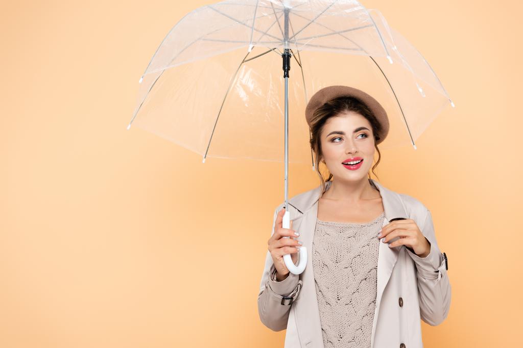 トレンチコートとベレー帽のファッショナブルな女性離れて桃の上に透明な傘の下で - 写真・画像