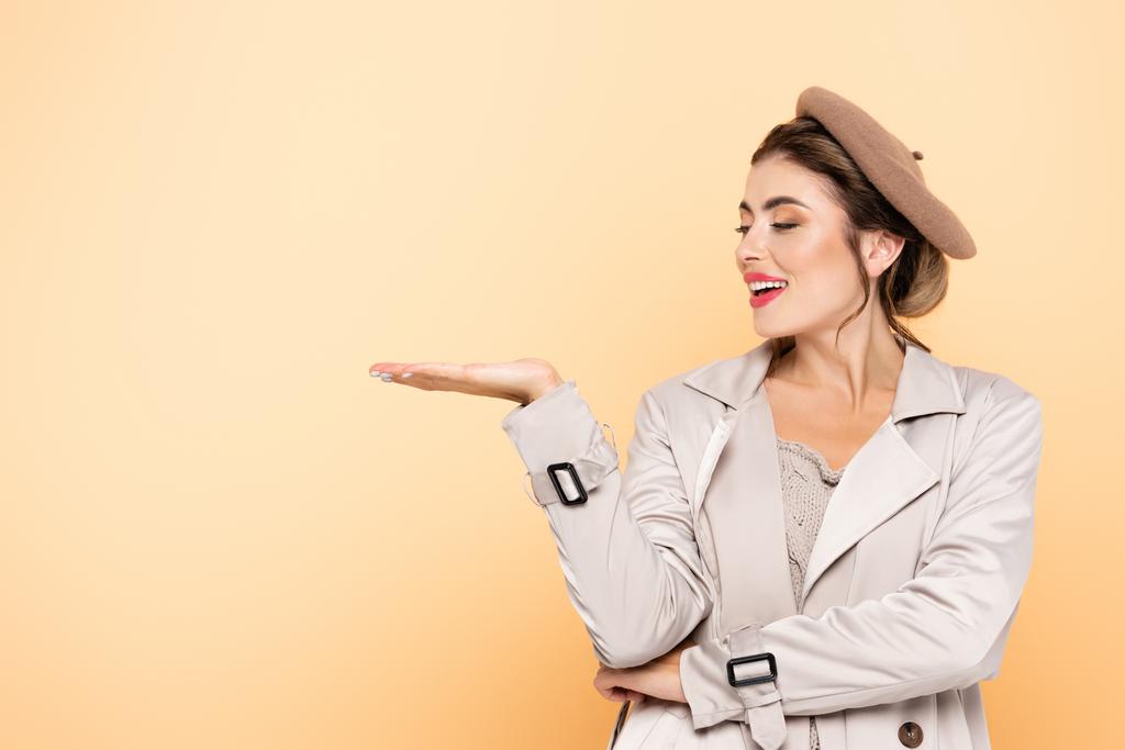 стильная женщина в пальто и берете указывает рукой на персик - Фото, изображение