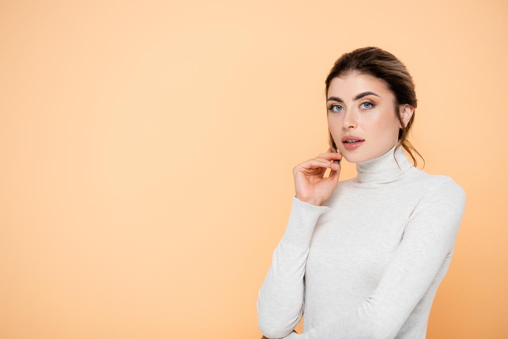 stylish woman in turtleneck holding hand near face isolated on peach  - Photo, Image