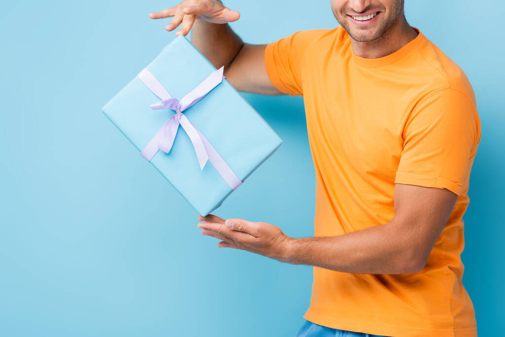 обрезанный вид счастливого человека в футболке с завернутой подарочной коробкой на синем - Фото, изображение