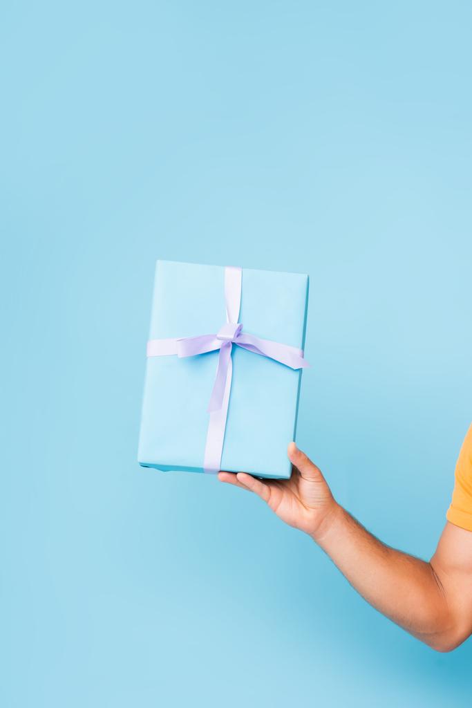 vista ritagliata di uomo in possesso di scatola regalo avvolto su blu - Foto, immagini