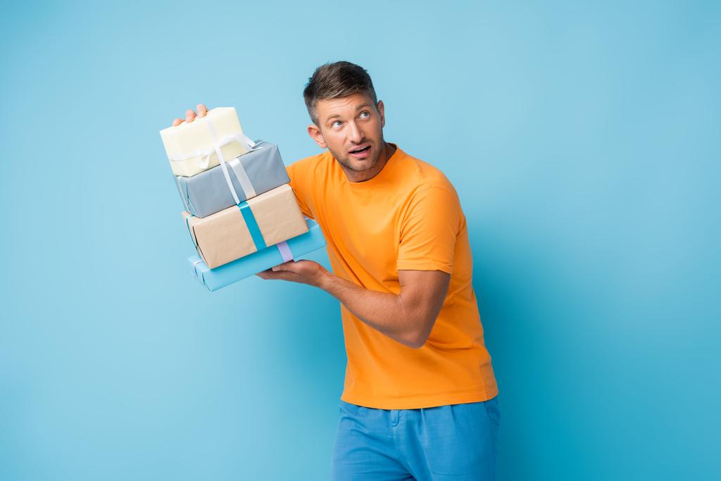 Tişörtlü meraklı bir adam elinde hediyelerle mavi gözlerden uzaklaşıyor. - Fotoğraf, Görsel