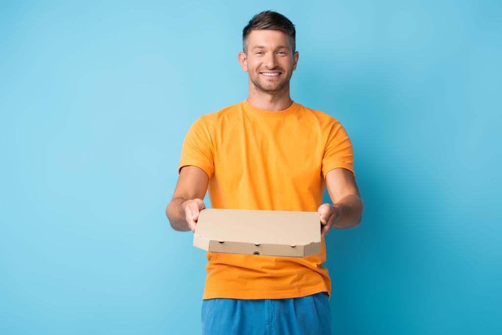Χαρούμενος άνδρας με t-shirt κρατώντας χάρτινο κουτί πίτσας στο μπλε - Φωτογραφία, εικόνα