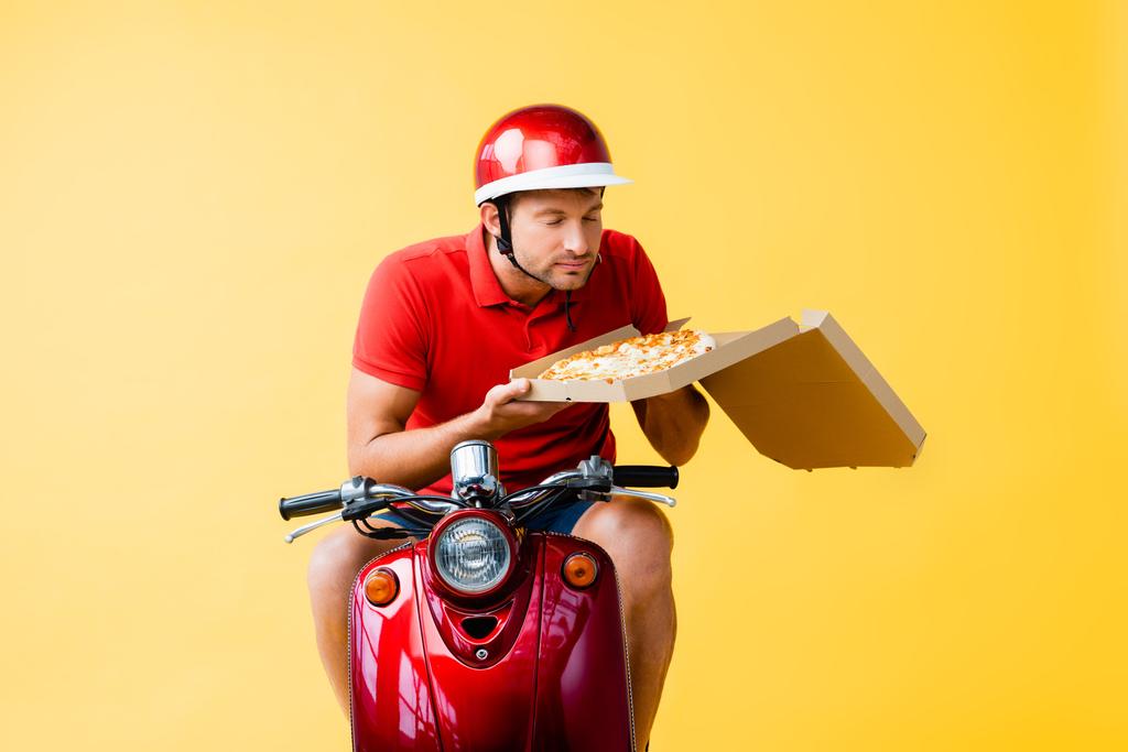 dostawca w kasku jazda na czerwonym skuterze i zapach pizzy w pudełku na żółtym - Zdjęcie, obraz