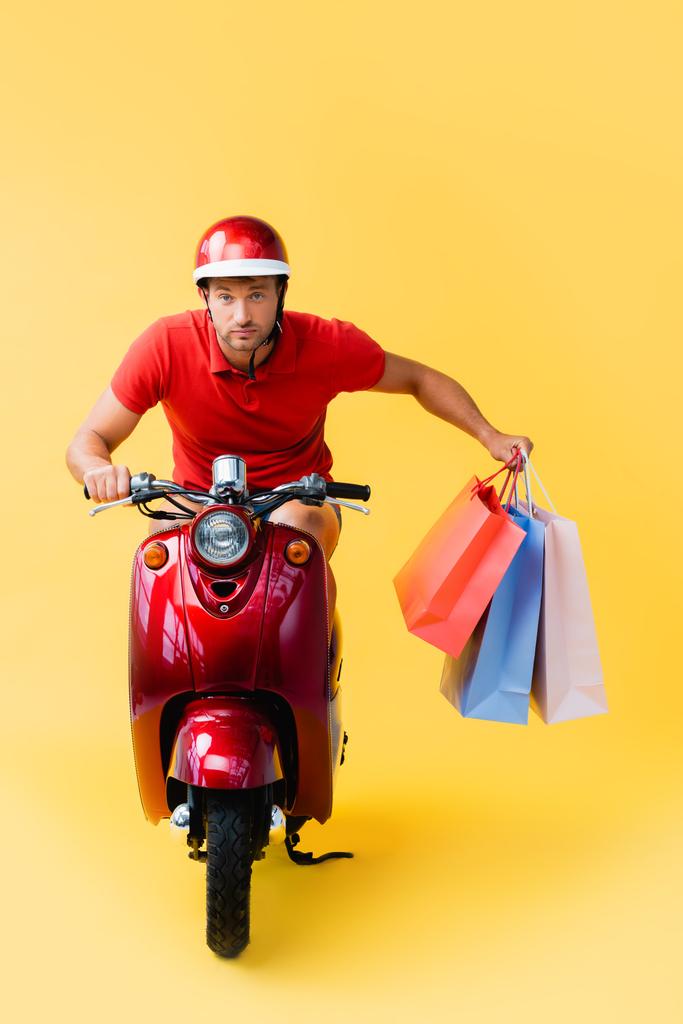 repartidor en casco a caballo scooter y llevar bolsas de compras en amarillo  - Foto, Imagen