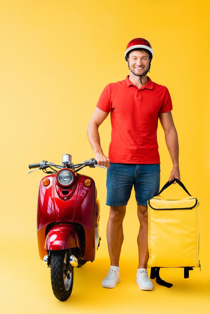 повна довжина веселого чоловіка з рюкзаком, що стоїть біля червоного скутера на жовтому
 - Фото, зображення