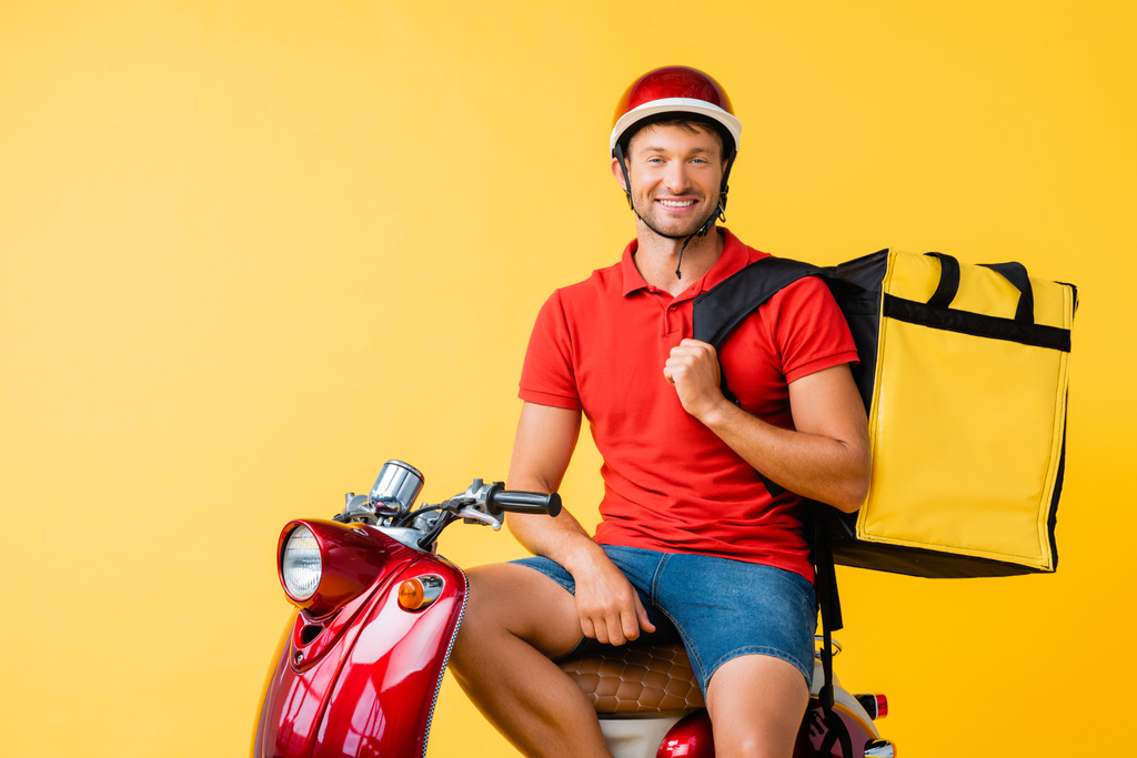 felice uomo di consegna con zaino seduto su scooter rosso su giallo - Foto, immagini